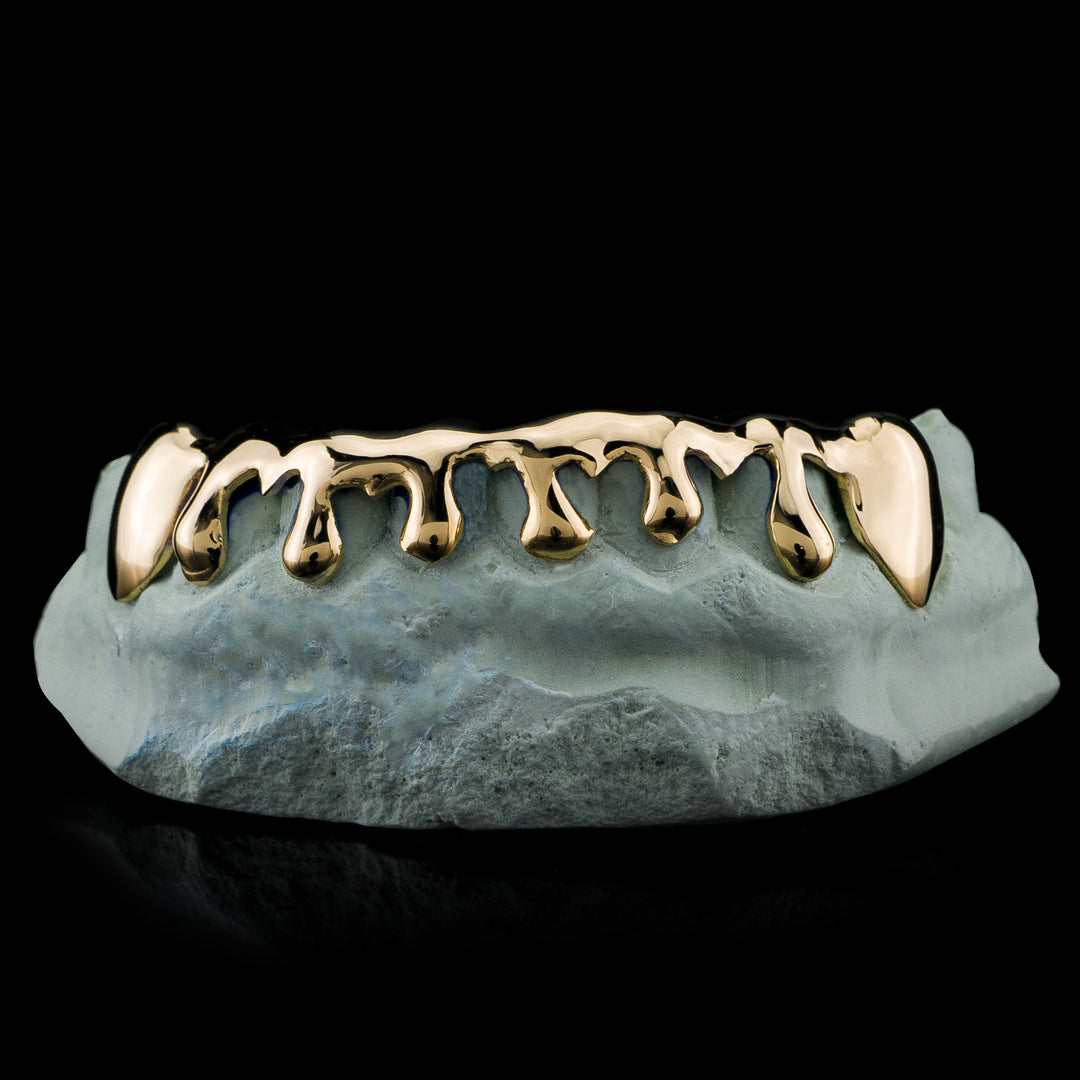 Gold-tone lower grillz with rounded drip-shaped edges and pointed end caps, displayed on a dental model.